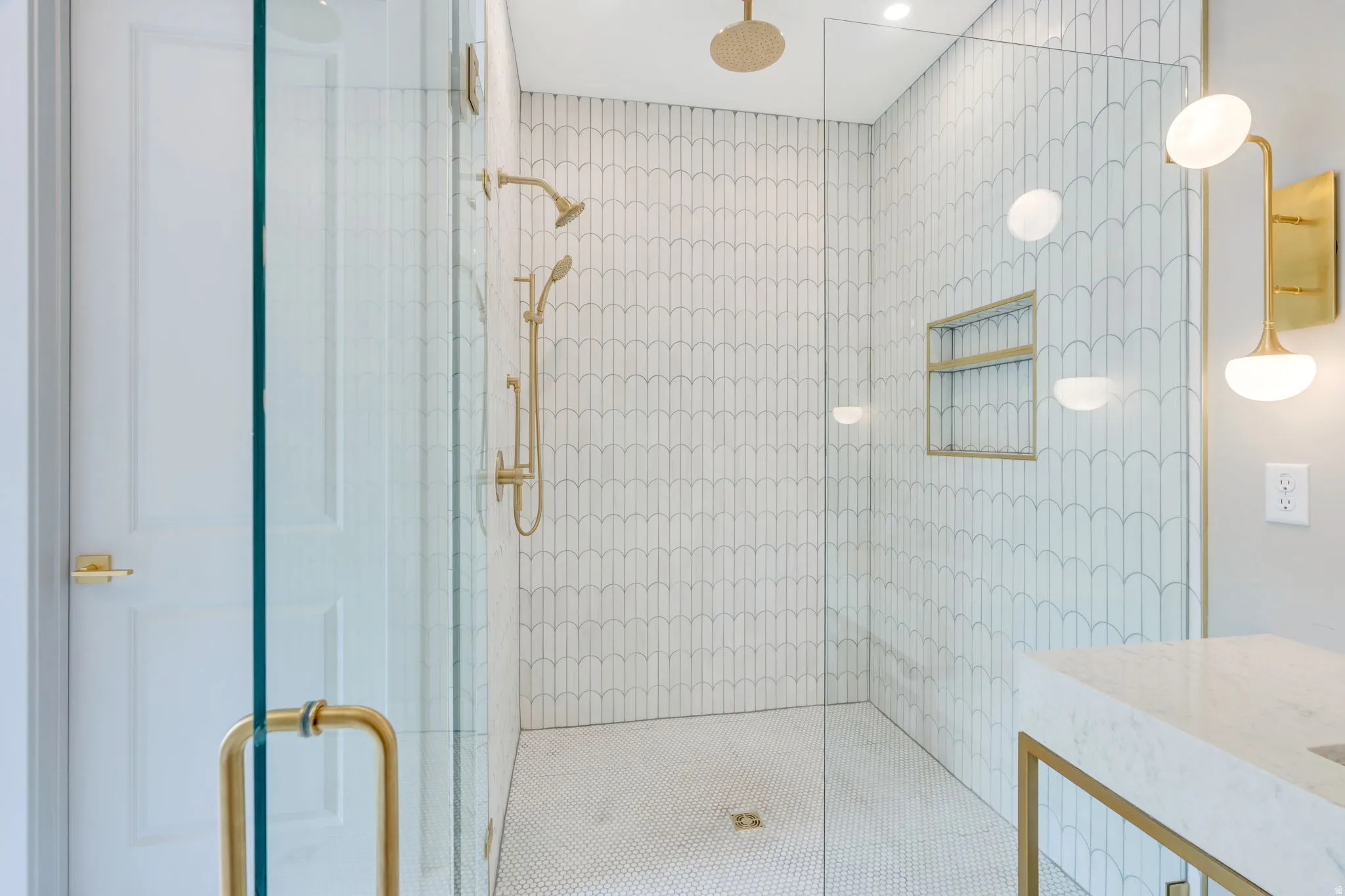 Glass-enclosed shower featuring white scallop-patterned wall tile and a gold rain shower head