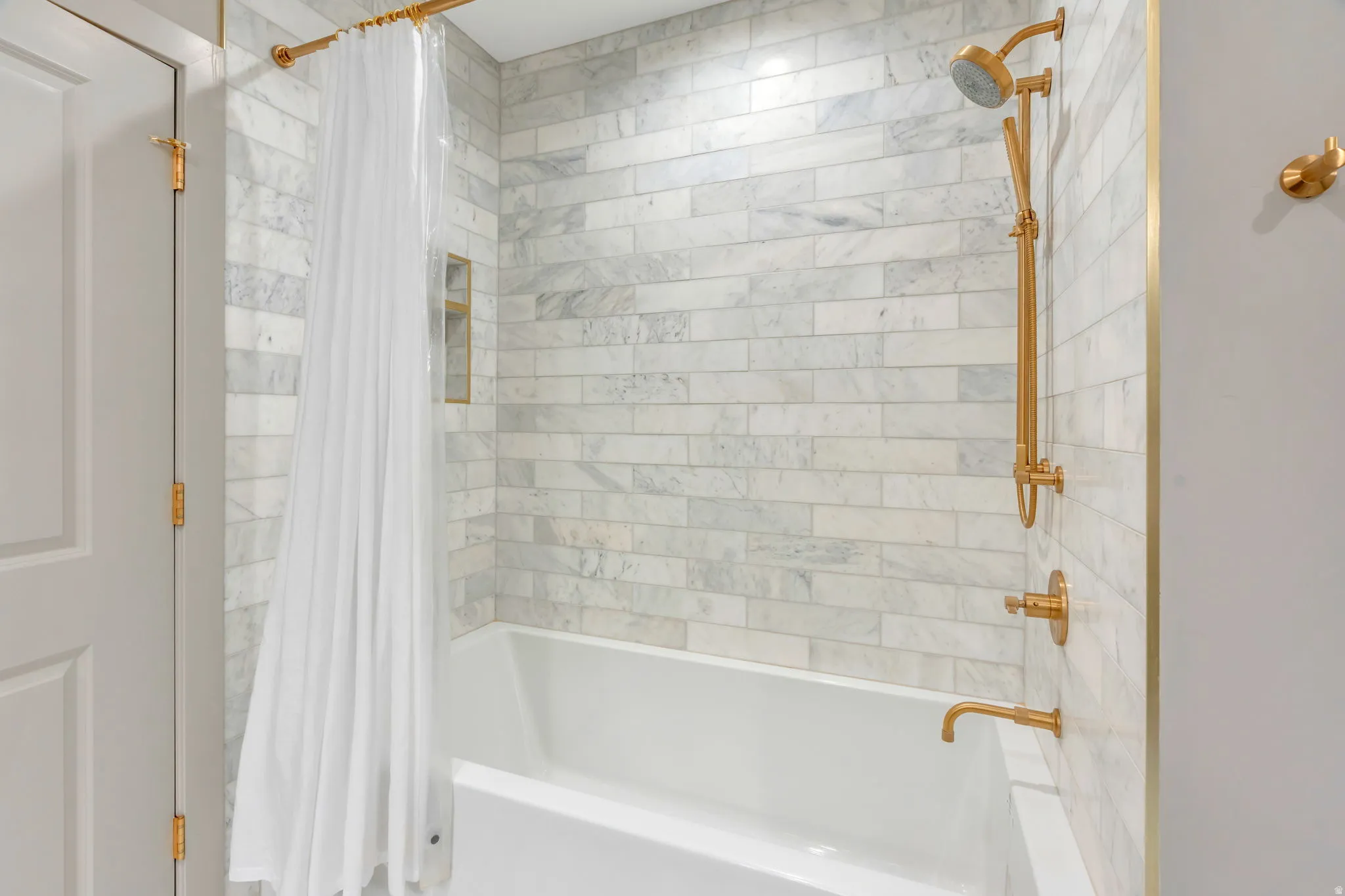 Bathtub with subway-style tile surround, featuring brass fixtures and a built-in shower niche