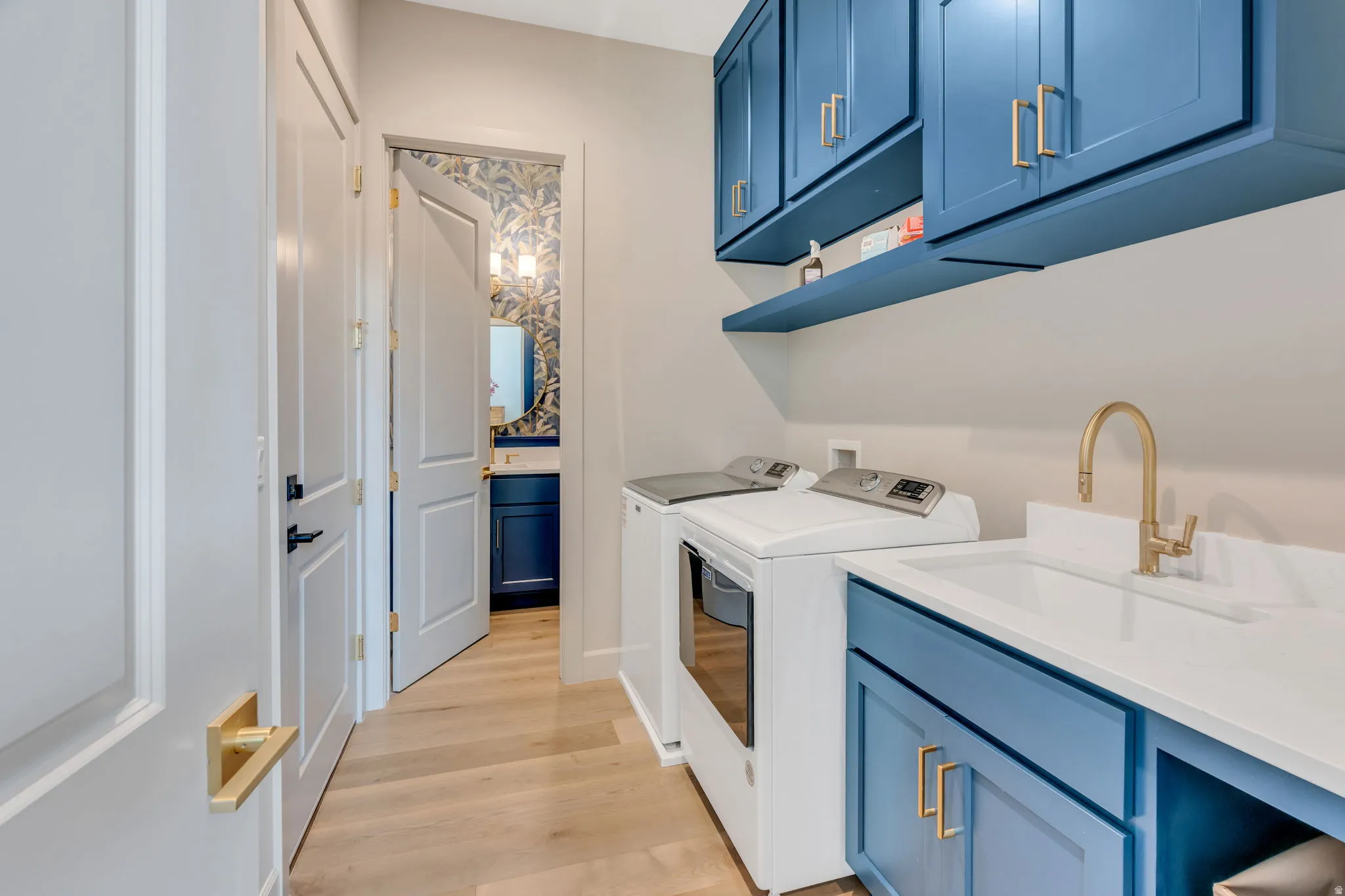 Laundry area featuring a built-in utility sink with gold-tone faucet, blue cabinetry with gold-tone hardware, and wood-finish flooring