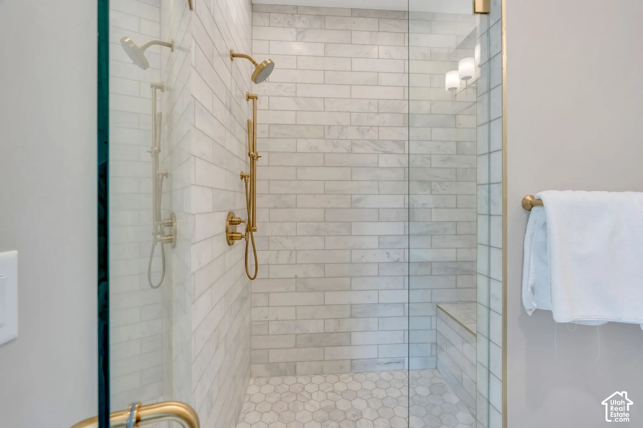 Glass-enclosed shower featuring white subway tile, a built-in bench, hexagonal floor tiles, a dual shower head system, and brass fixtures
