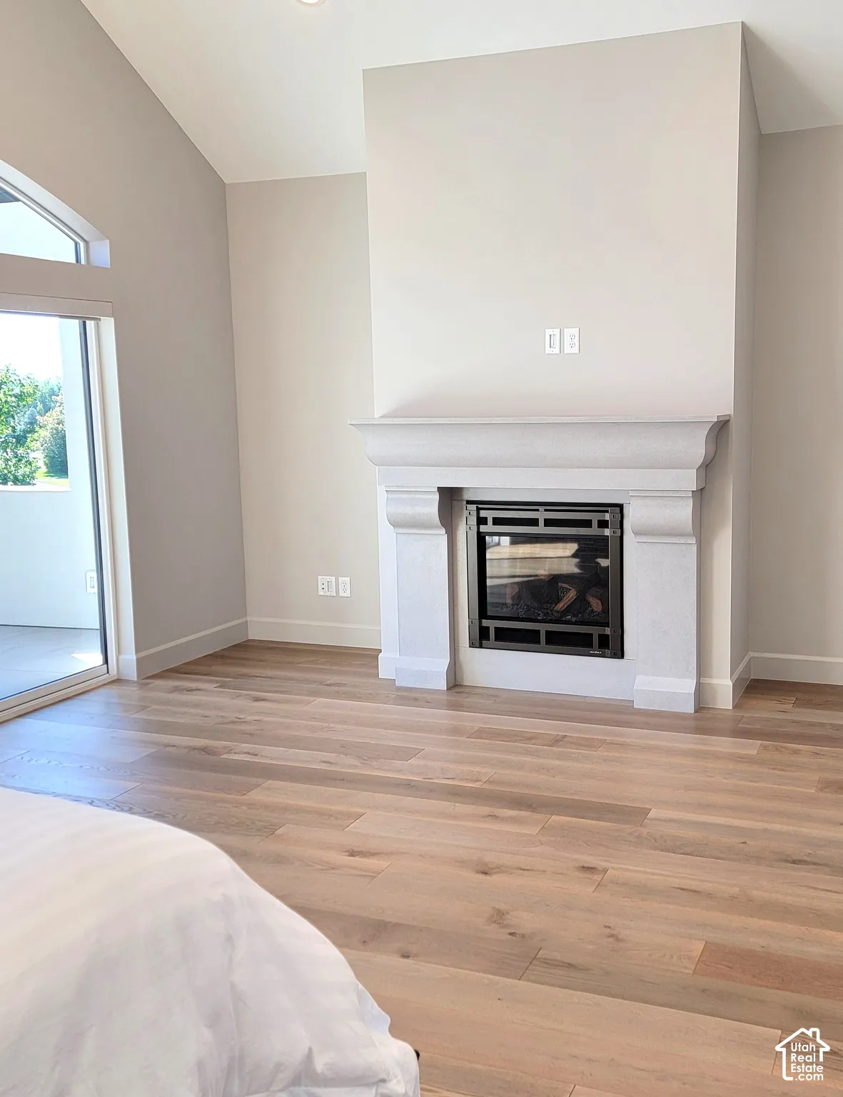 Vaulted ceilings, wood-finish flooring, and a stone-surround fireplace with a custom mantle, complemented by expansive windows and sliding glass door access