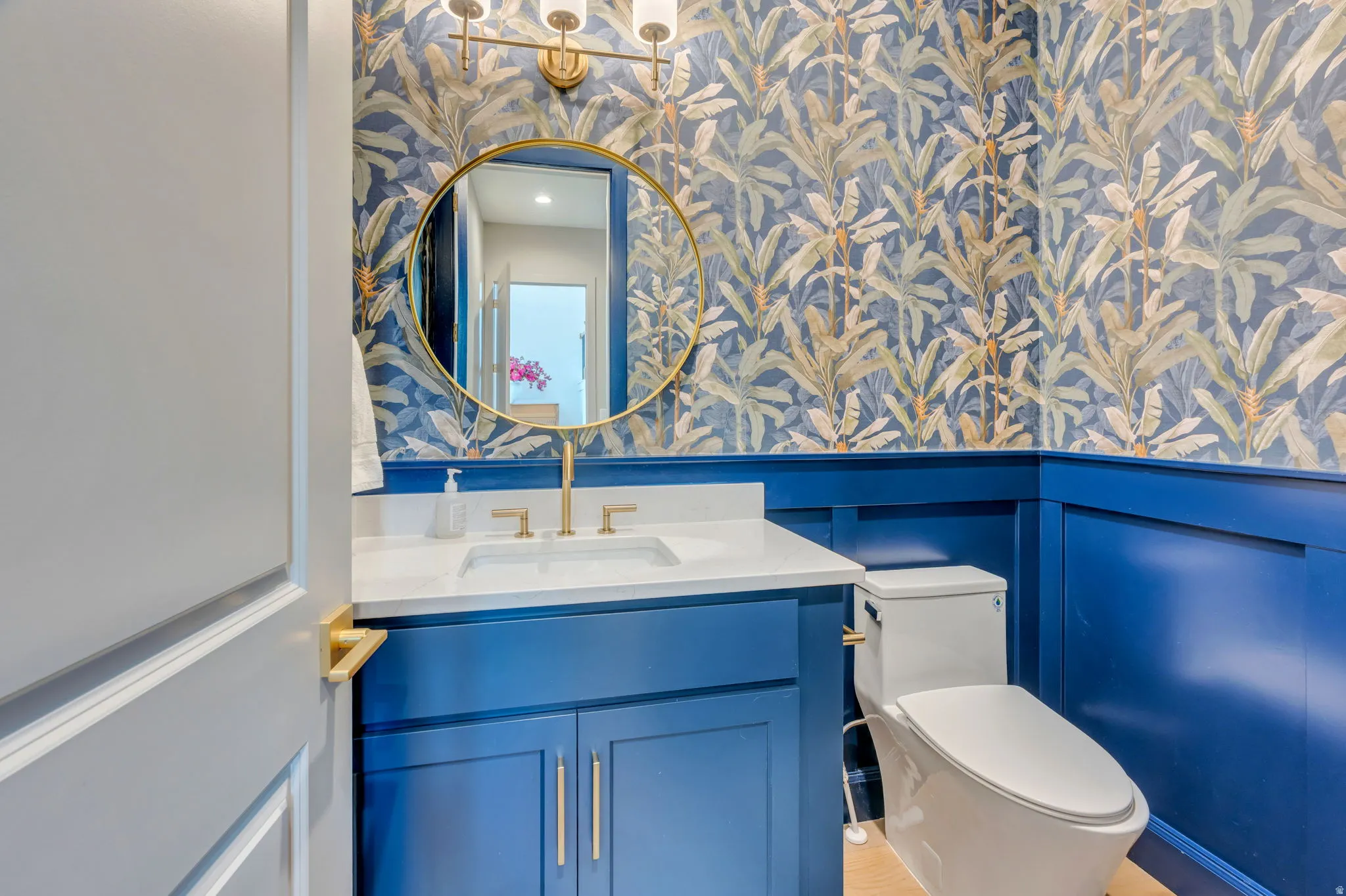 Vanity with a white countertop and gold-finish faucet, paired with a round gold-finish mirror