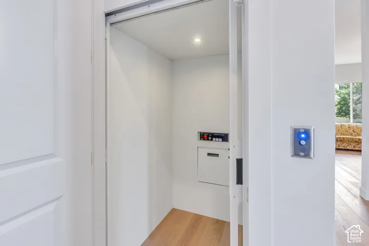 Interior residential elevator featuring light wood-finish flooring, recessed lighting, and a control panel