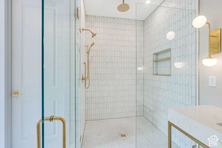 Glass-enclosed shower featuring white scallop-patterned wall tile and a gold rain shower head