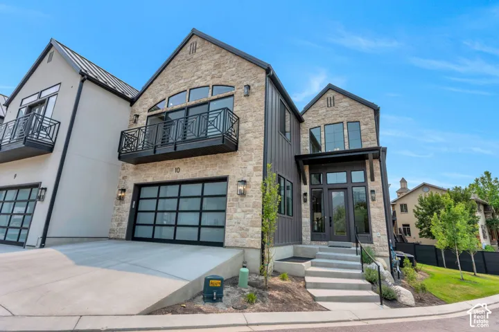 Contemporary stone and vertical siding exterior with a prominent arched window and a private balcony featuring a decorative metal railing