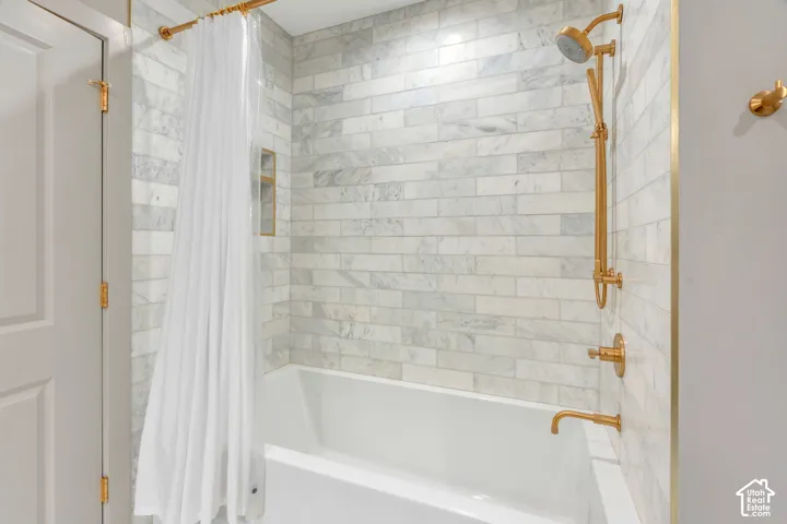 Bathtub with subway-style tile surround, featuring brass fixtures and a built-in shower niche