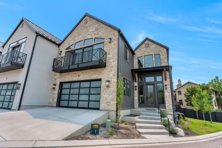 Contemporary stone and vertical siding exterior with a prominent arched window and a private balcony featuring a decorative metal railing