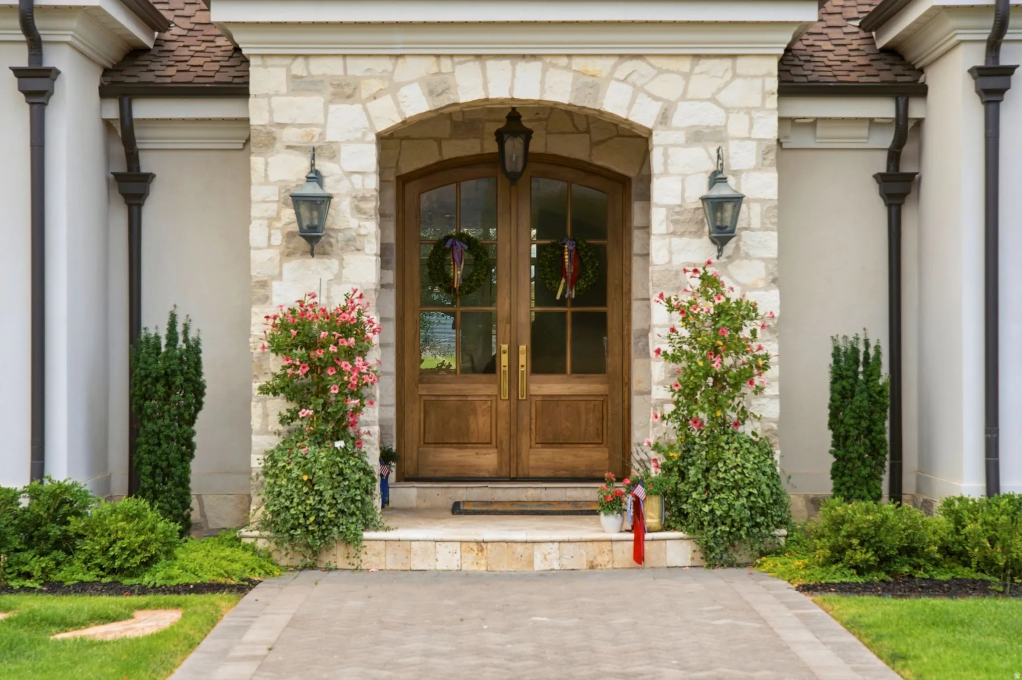 Arched wooden entry doors with glass panels, flanked by stone masonry and sconce lighting