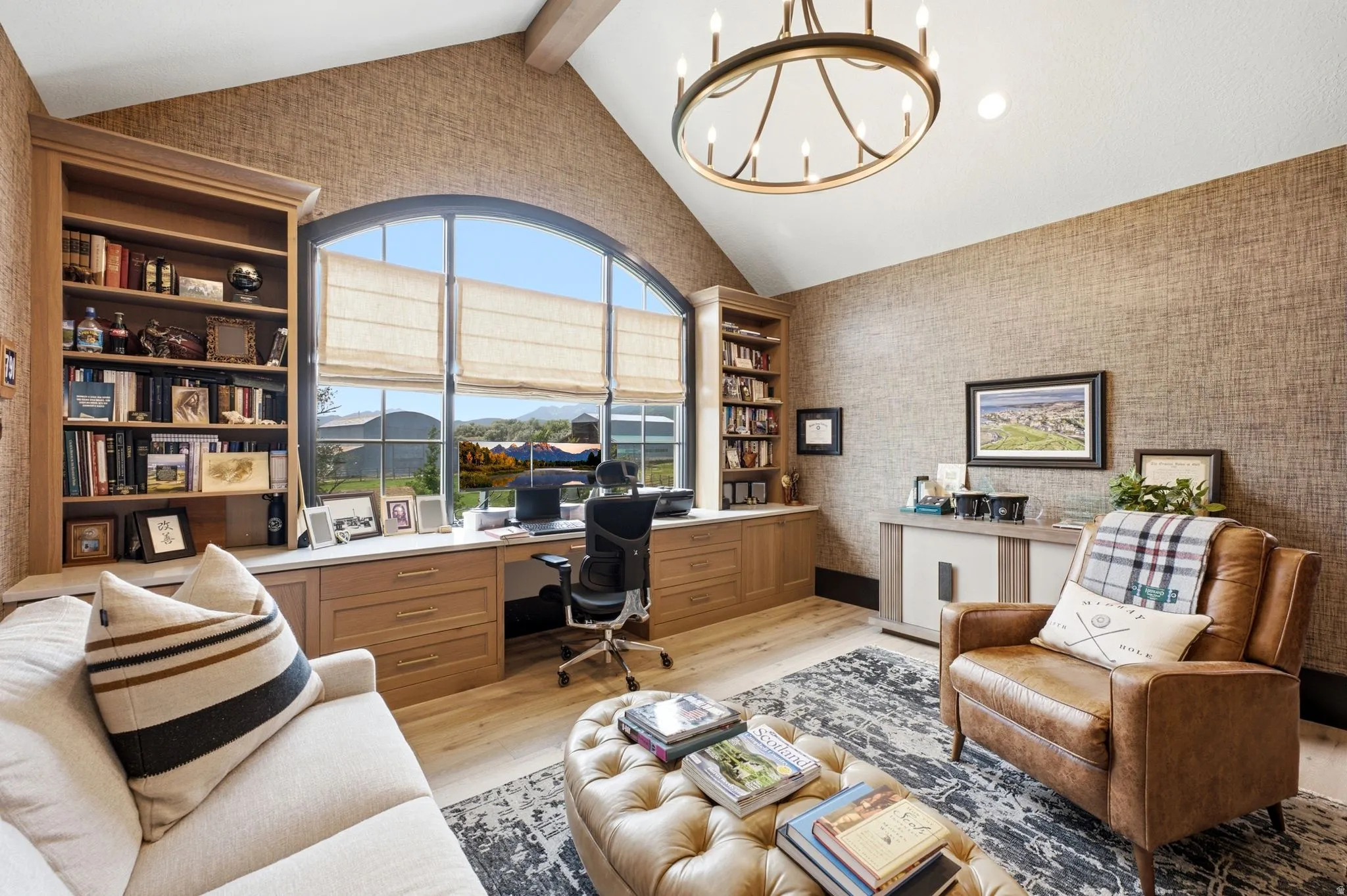 Vaulted ceiling office space featuring a large arched window, built-in cabinetry, wood-finish flooring, and a circular chandelier