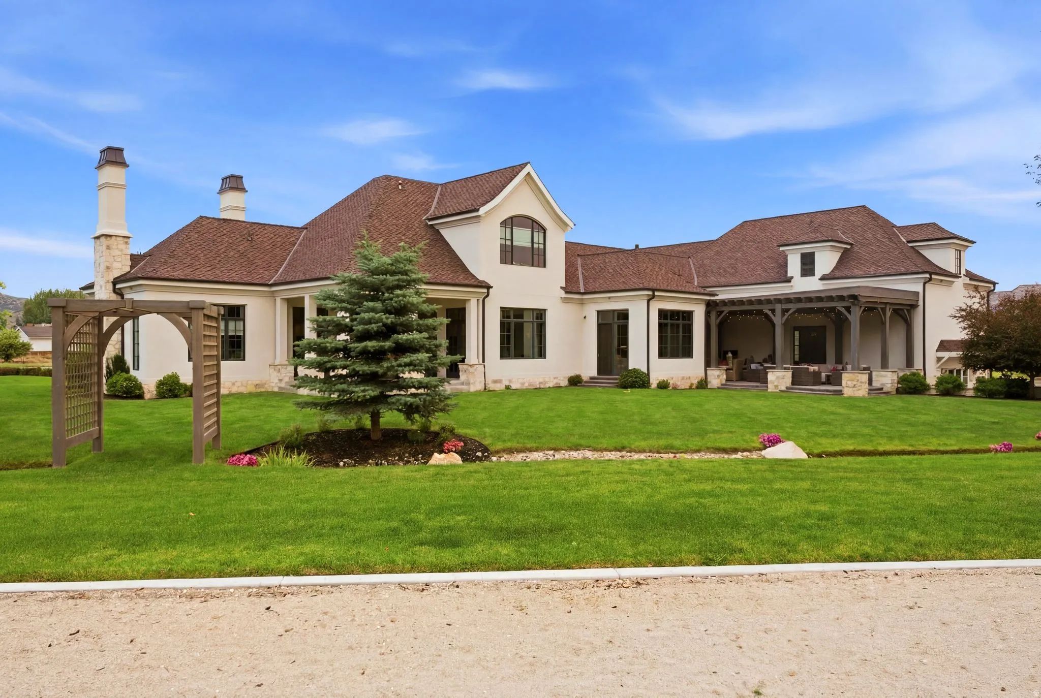 Expansive rear facade featuring a covered patio, multiple dormer windows, and a rich brown shingle roof