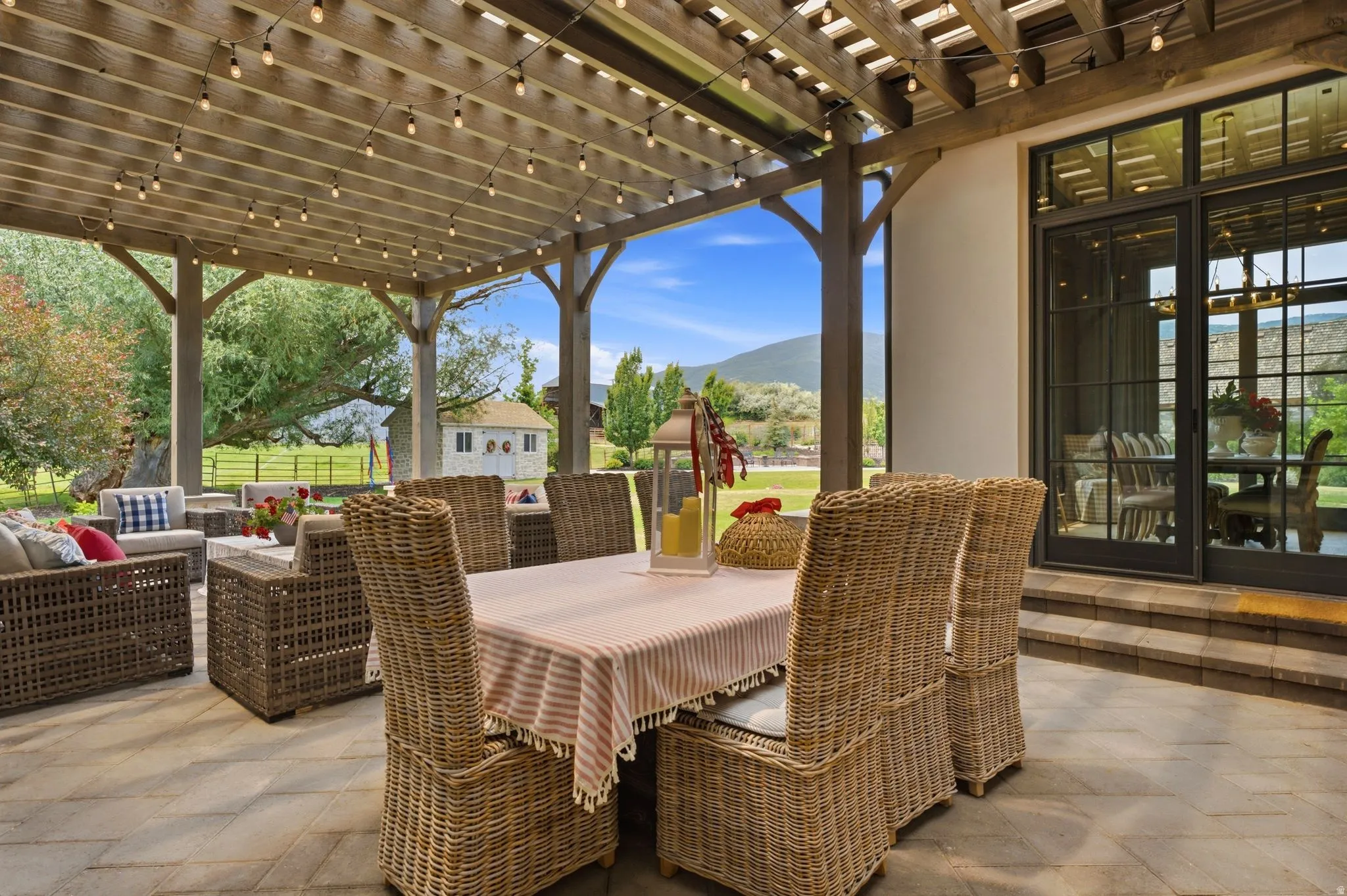 Expansive outdoor patio featuring a wood pergola, string lighting, and direct access to interior spaces through large glass doors
