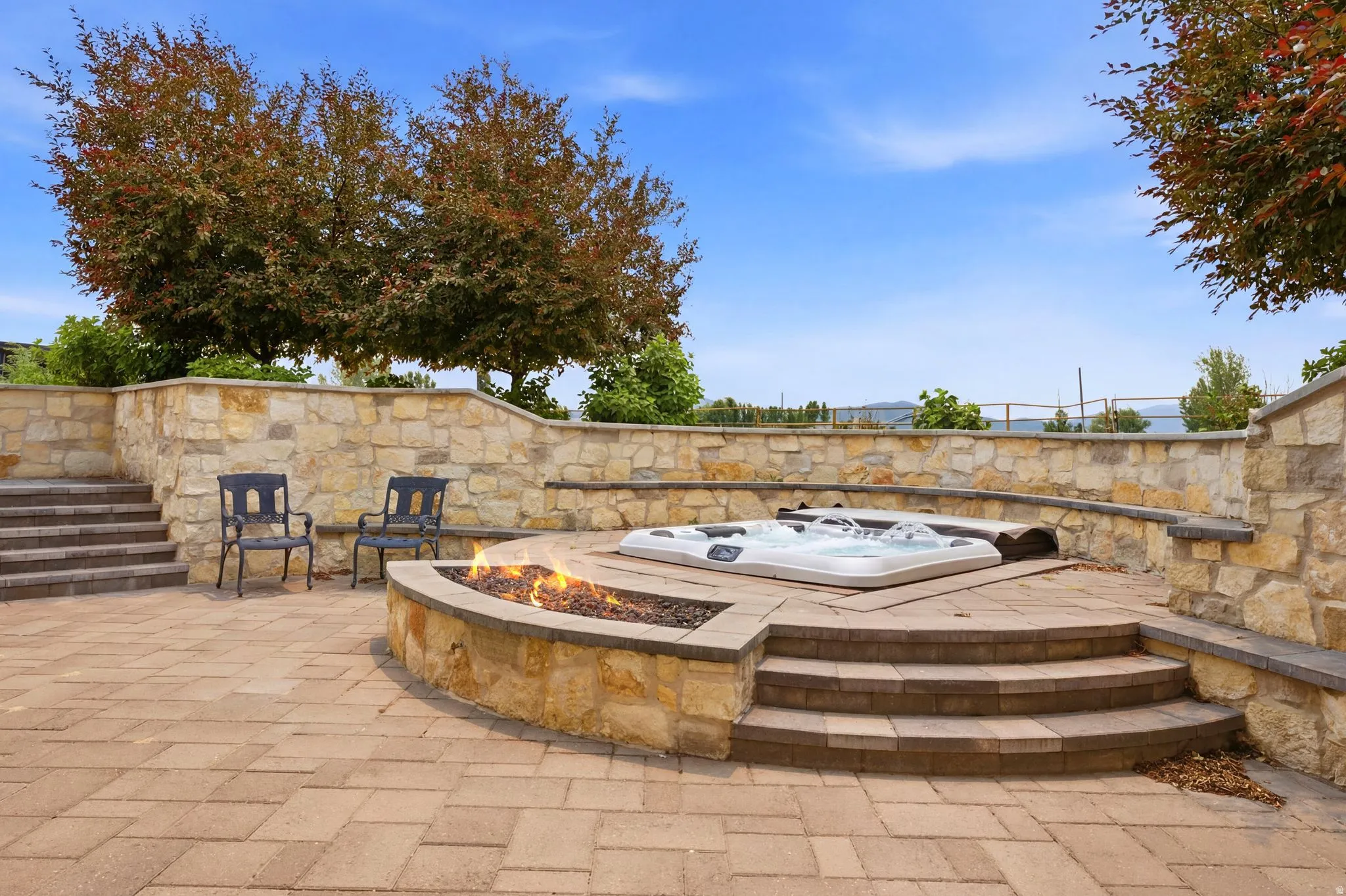 Spacious paver patio featuring a built-in fire pit, integrated hot tub, and stacked stone retaining walls