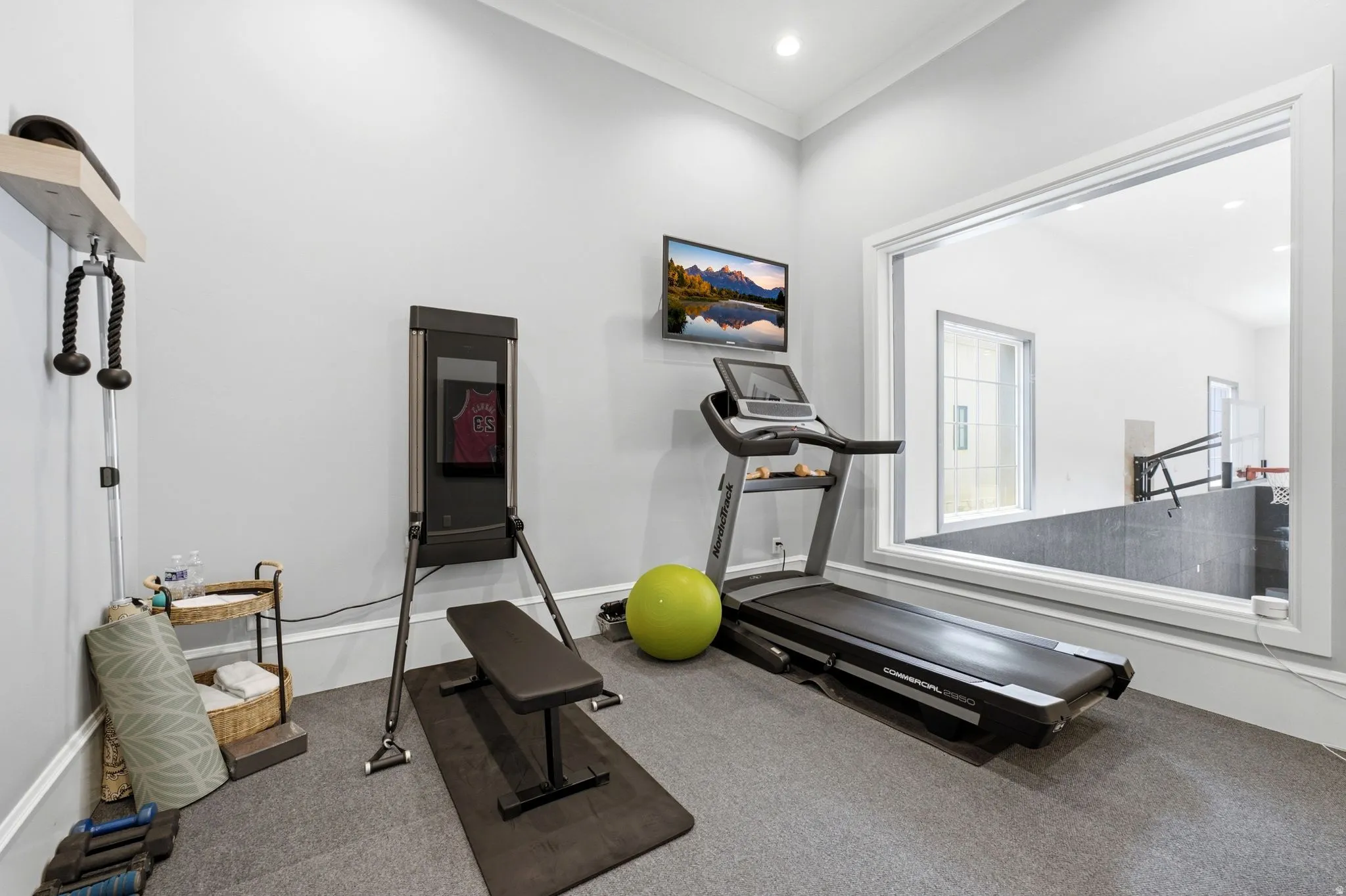 Dedicated fitness space featuring light gray walls, crown molding, recessed lighting, and a large interior window