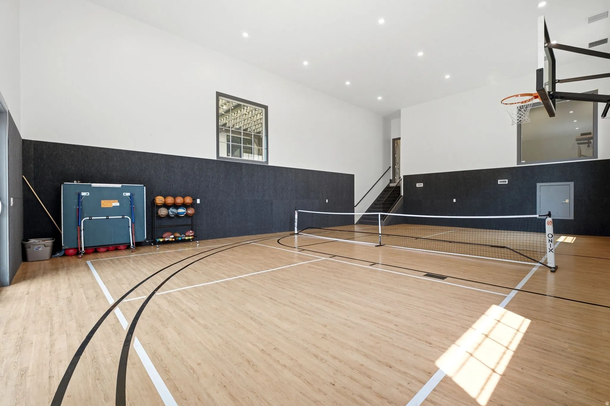 Indoor multi-sport court featuring wood-finish flooring with court markings, high ceilings, a basketball hoop, and recessed lighting
