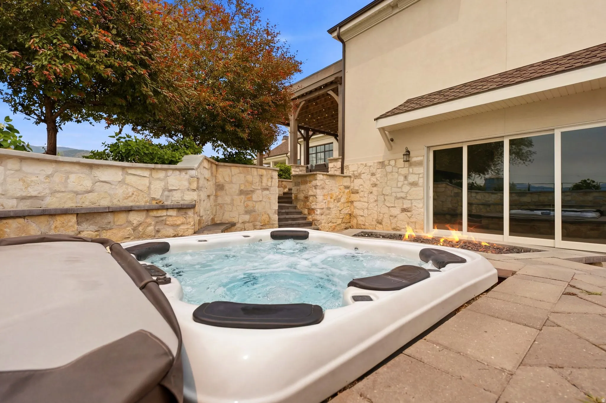 Outdoor hot tub with integrated seating, surrounded by paver patio and a linear fire feature