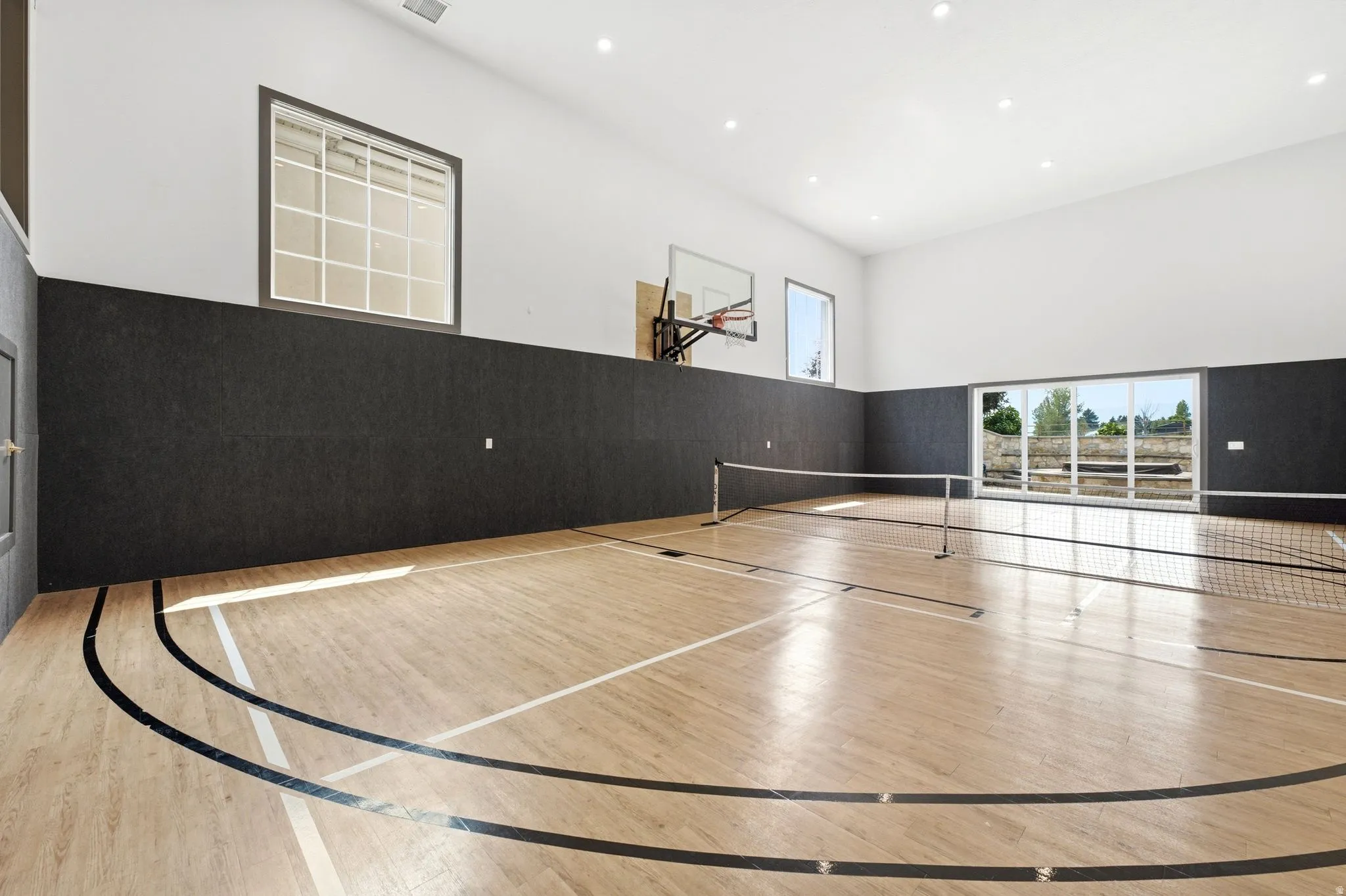 Indoor sports court featuring wood-finish flooring with court markings, high ceilings, recessed lighting, a basketball hoop, and multiple windows