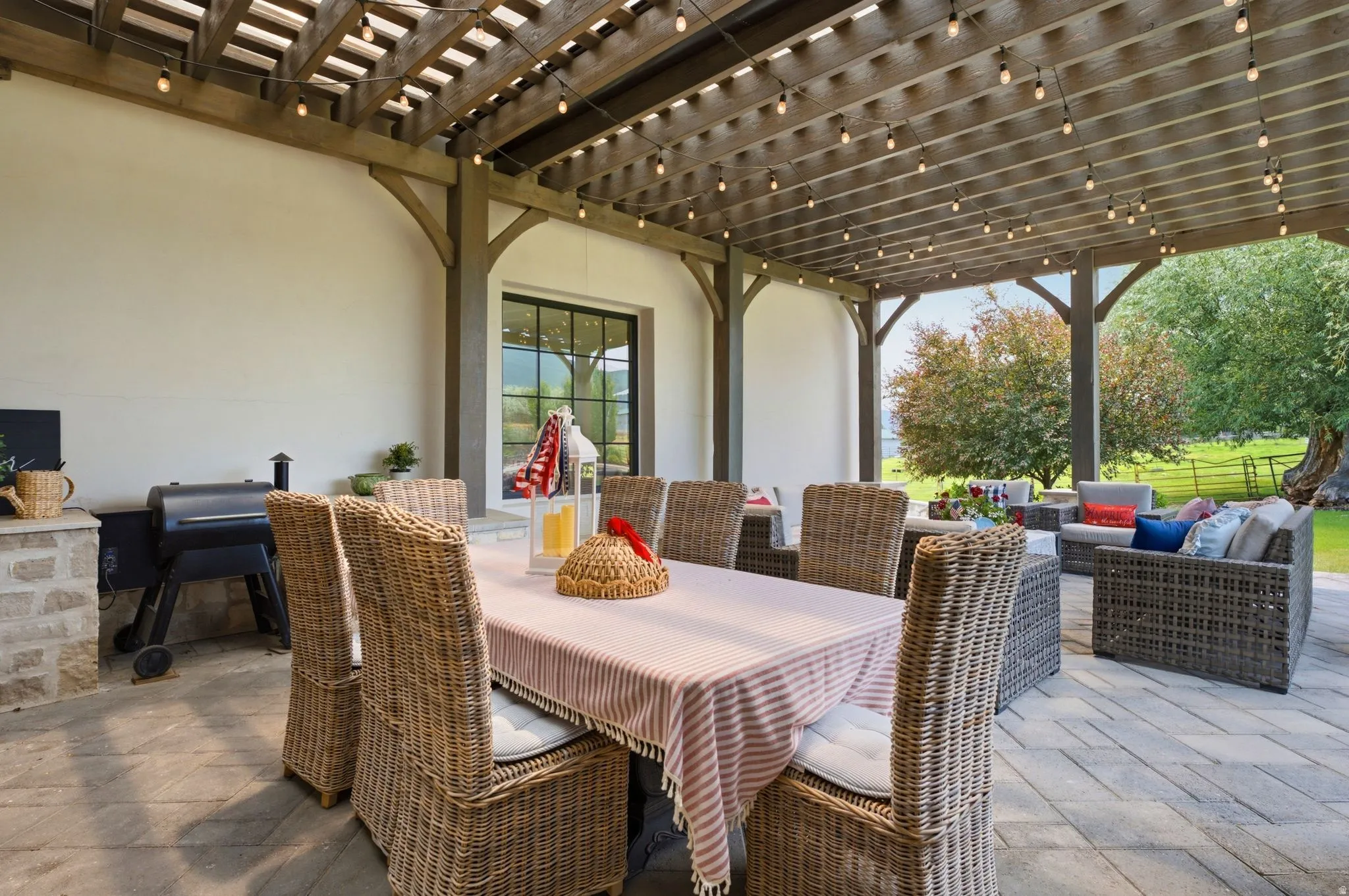 Expansive covered patio featuring a wood pergola with string lighting, stone-clad grilling station, and large format paver flooring