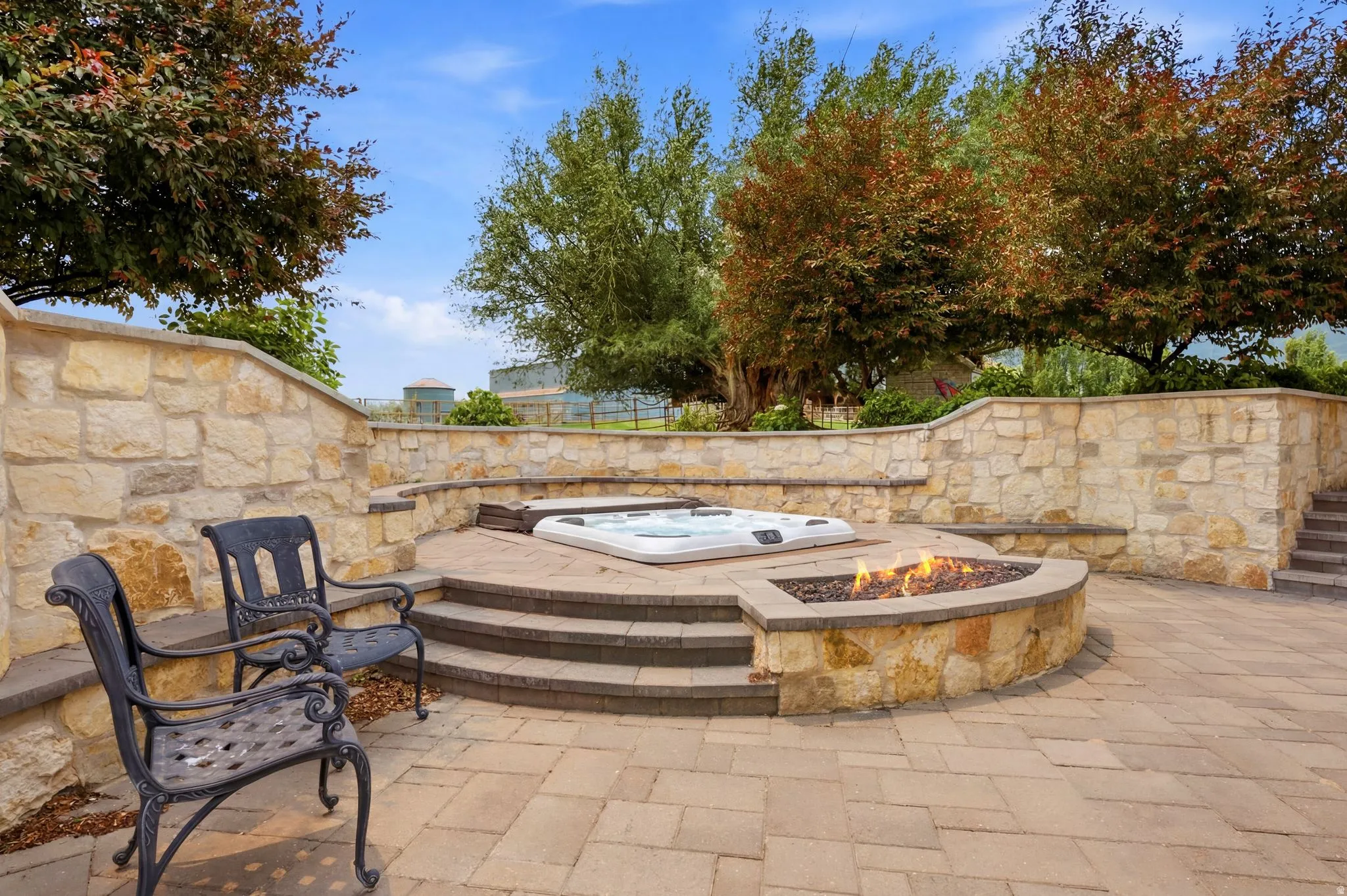 Expansive outdoor entertaining area featuring a built-in hot tub, a fire pit, and stone retaining walls