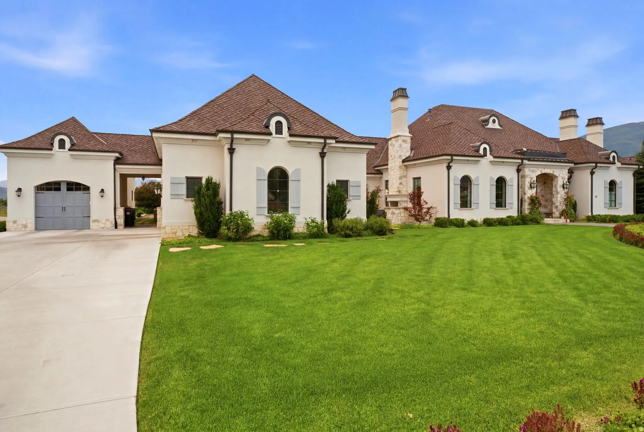 Expansive property featuring a stucco exterior with stone accents, a multi-gabled roof, arched windows with light-colored shutters, and multiple chimneys