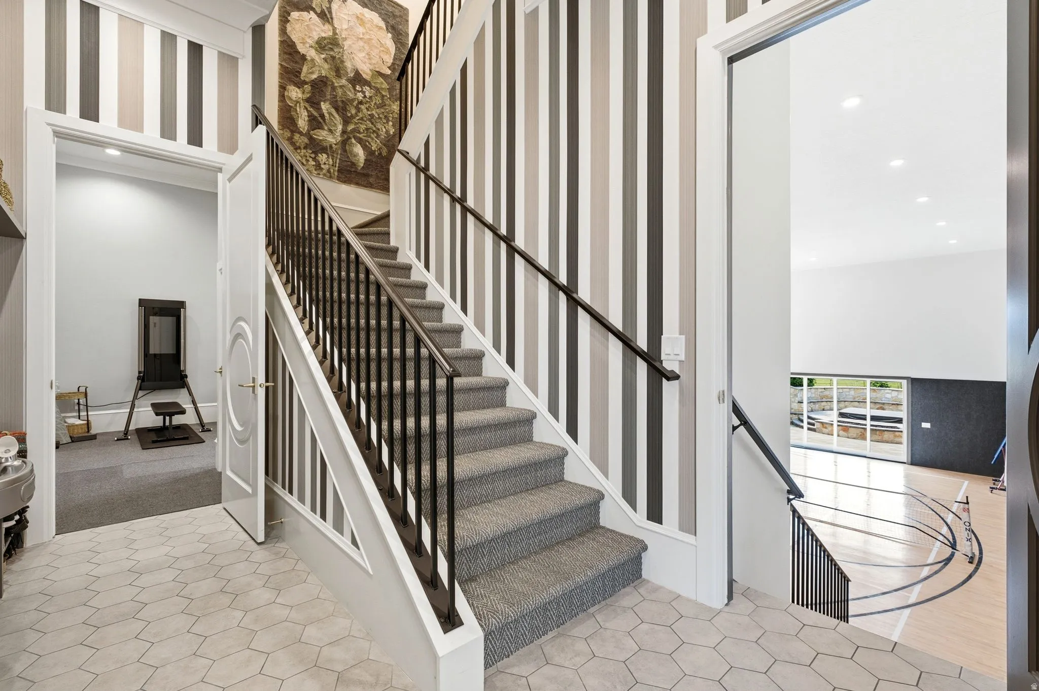 Staircase featuring carpeted treads, dark metal balusters, and a solid wood handrail, complemented by striped wallpaper