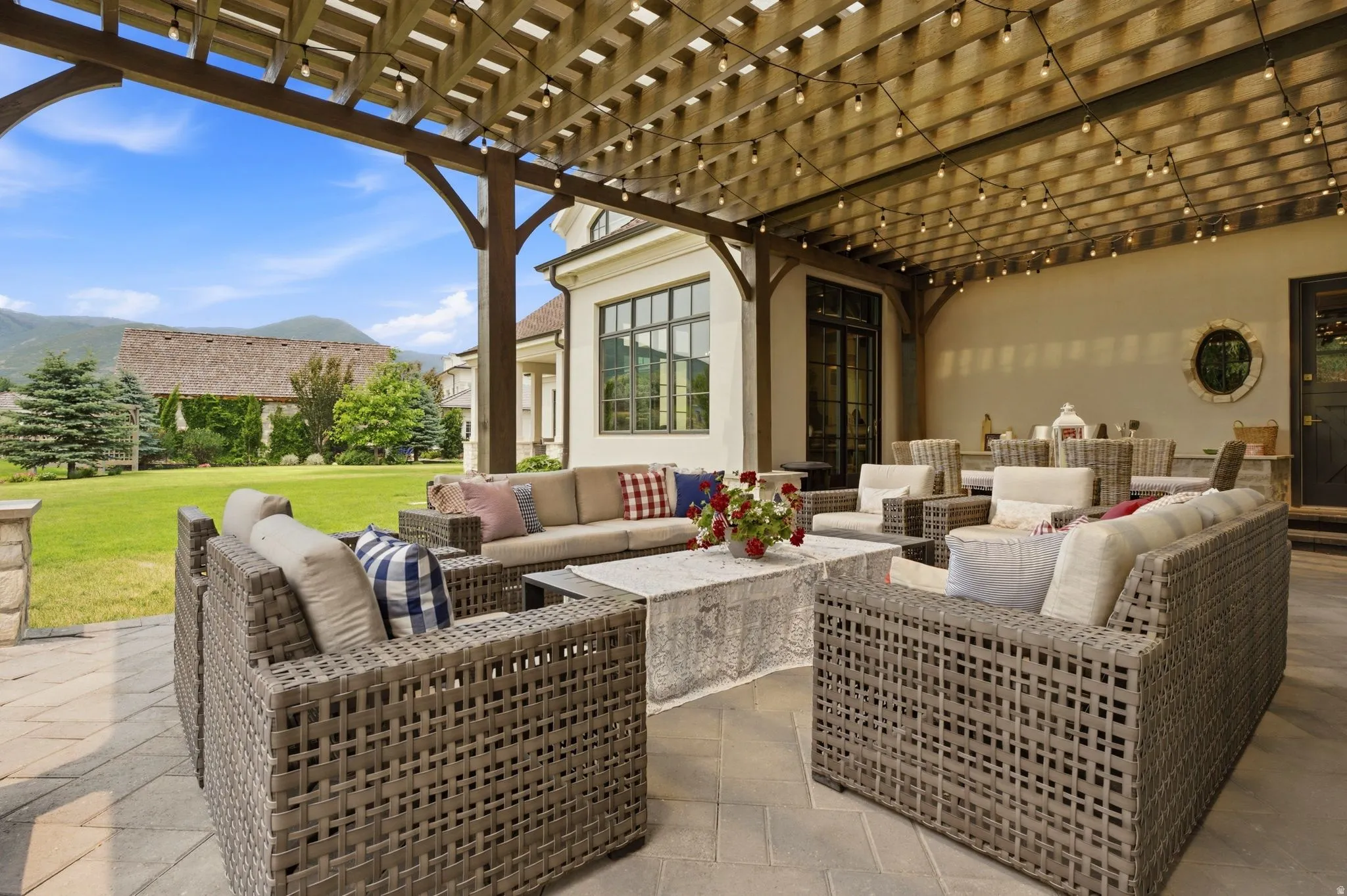 Expansive paver patio with a wooden pergola, string lighting, and ample seating areas