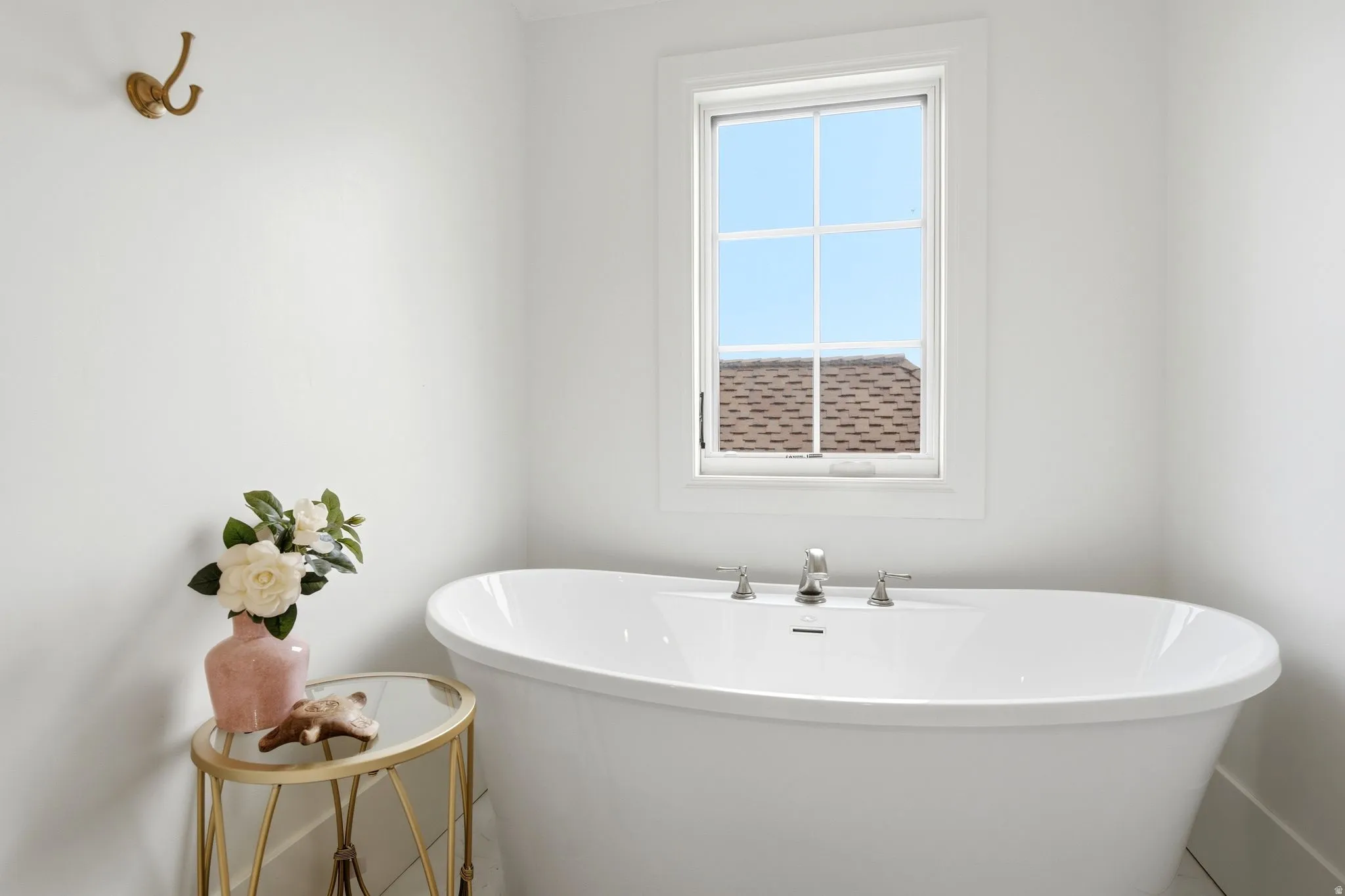 Freestanding soaking tub with polished chrome fixtures, set beneath a white-framed window