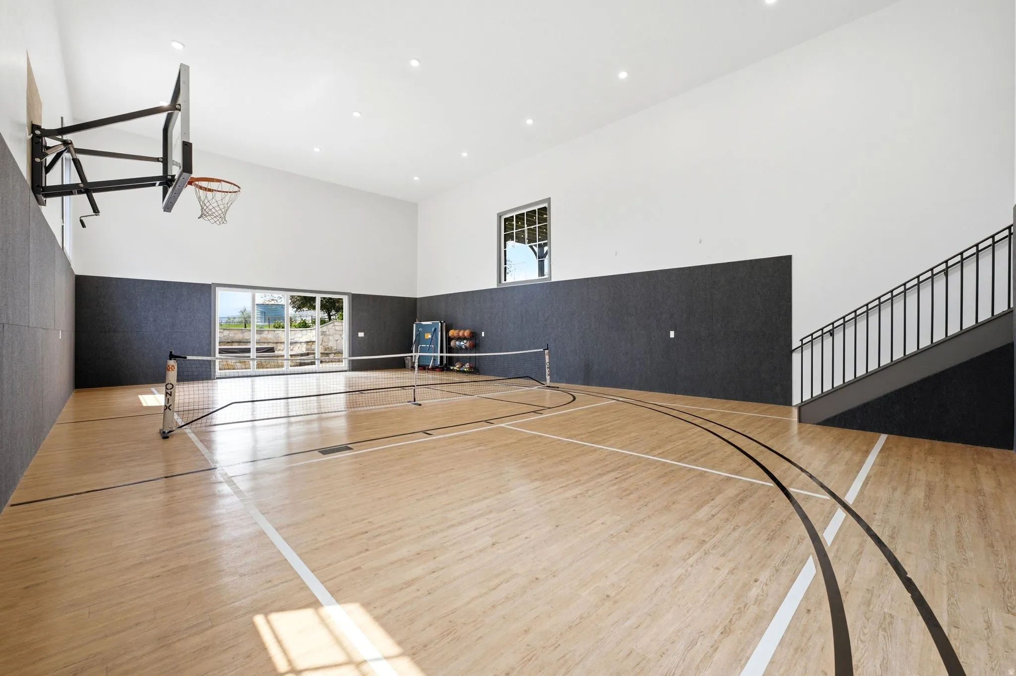 Indoor sports court featuring hardwood flooring with court markings, a basketball hoop, and a portable net