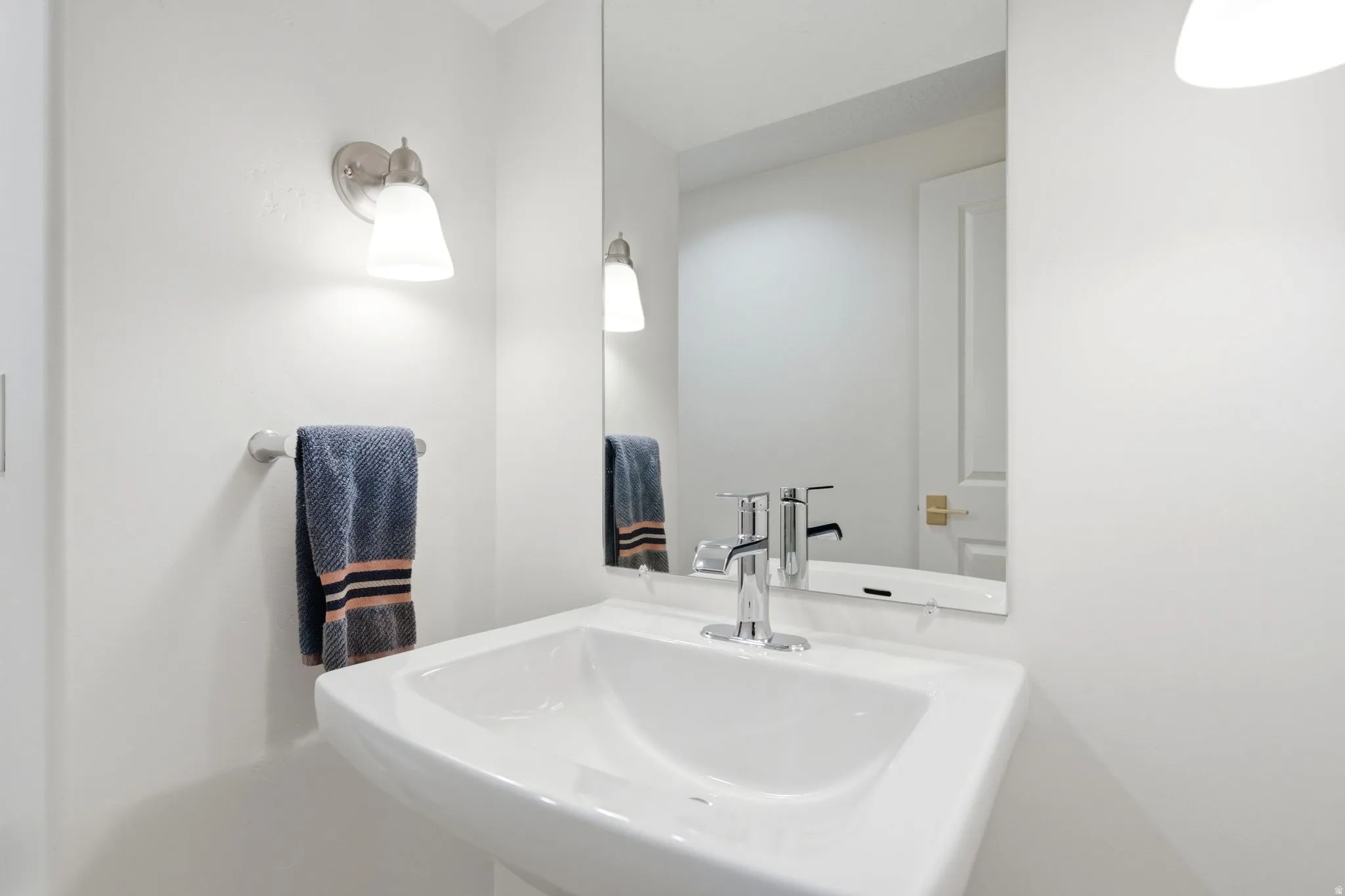 Pedestal sink with chrome faucet, framed mirror, and wall-mounted sconce lighting