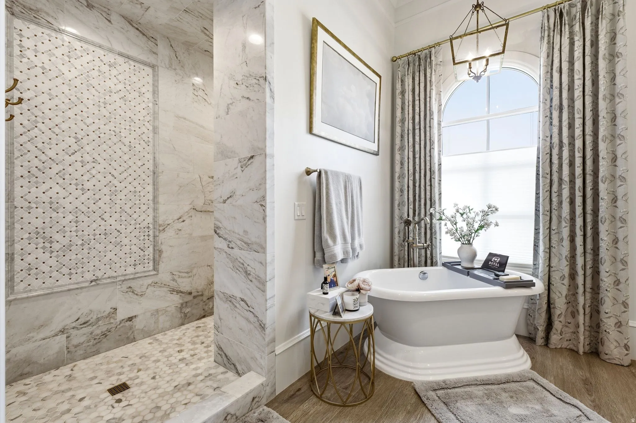 Freestanding pedestal bathtub with a large arched window, complemented by a spacious walk-in shower featuring patterned tile inlay, full-height tile walls, and hexagon tile flooring