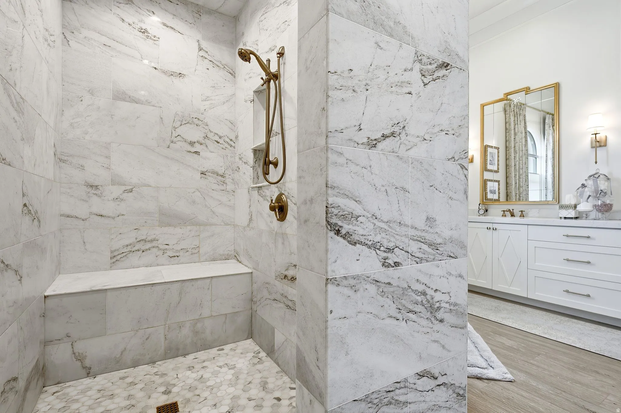 Spacious shower featuring full-height marble-look tile, a built-in bench, and a bronze-finish shower system