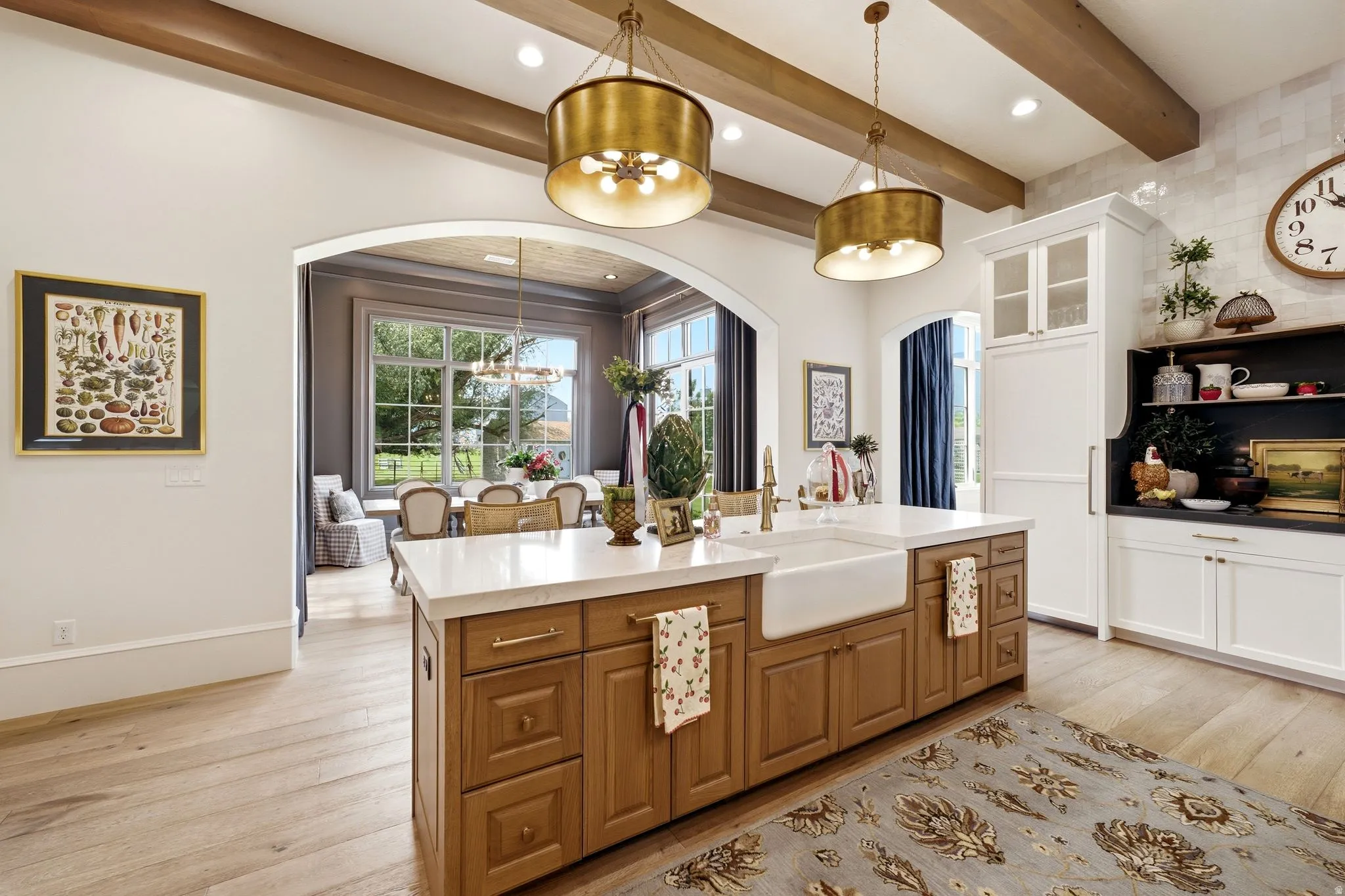 Gourmet kitchen featuring a large central island with an apron sink, wood-finish flooring, exposed ceiling beams, custom cabinetry, and integrated appliances