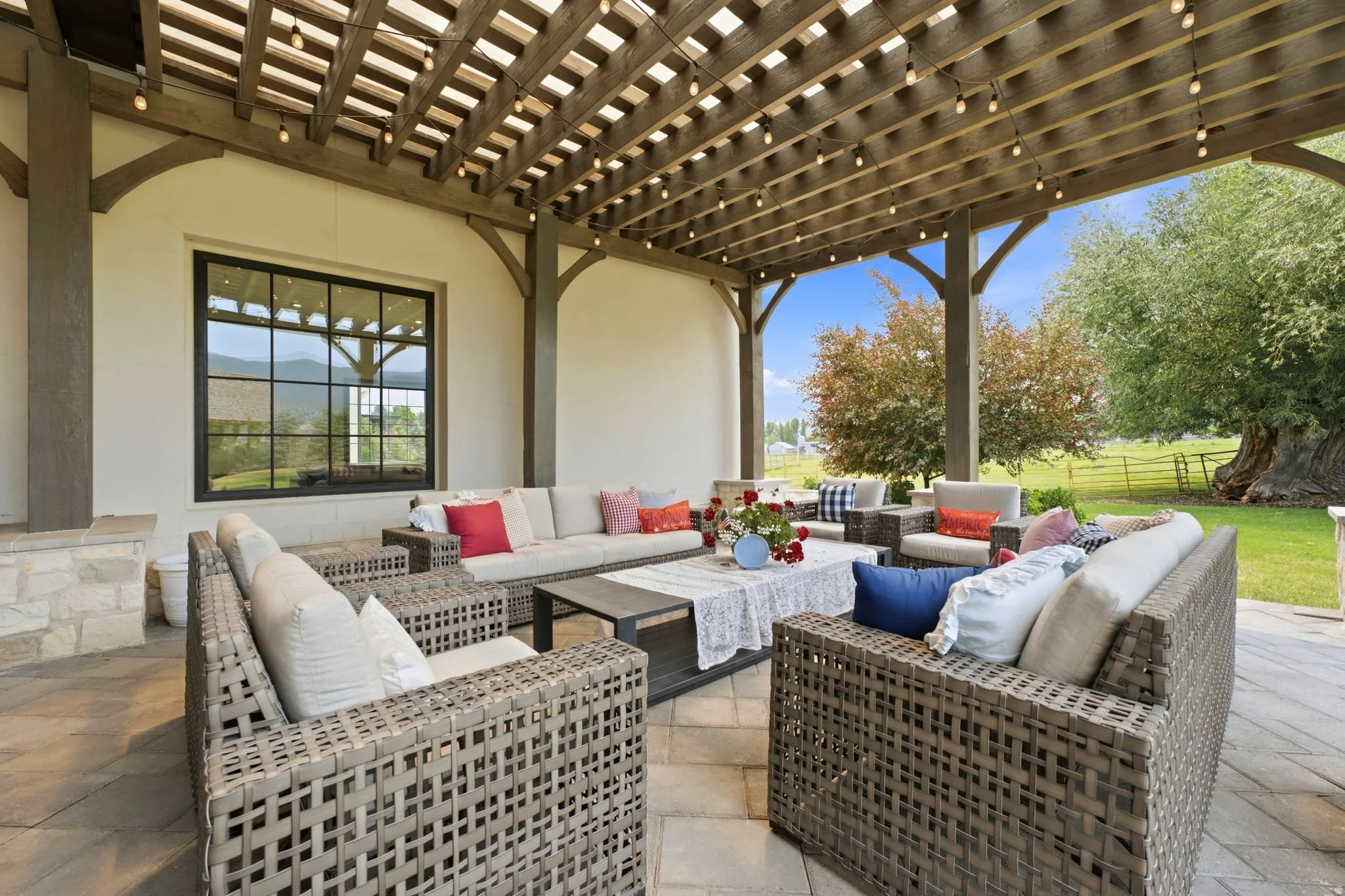 Expansive outdoor patio featuring a wood pergola with string lighting, stone veneer accents, and a large black-framed window