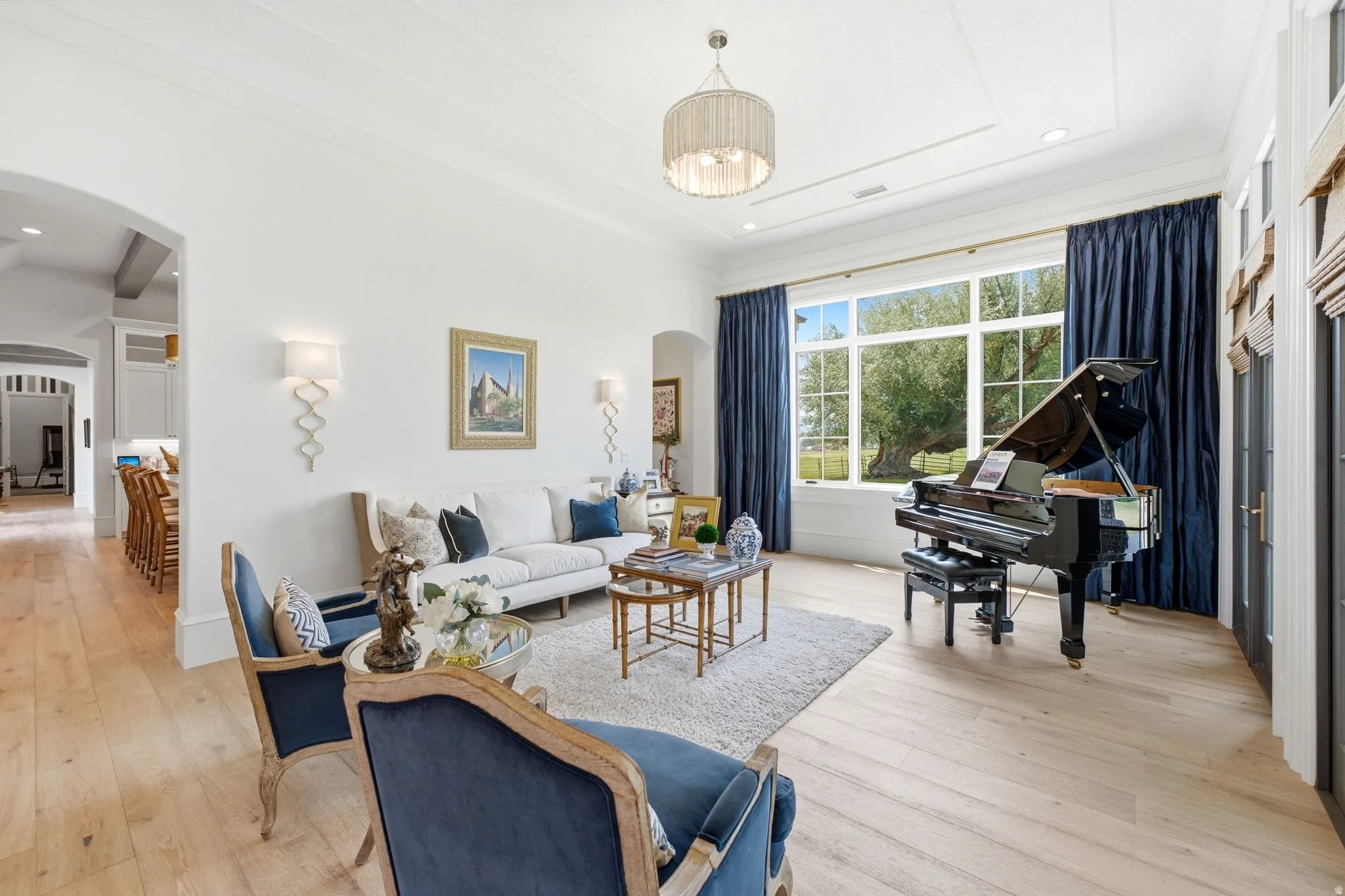 Bright living space featuring expansive windows, light wood-finish flooring, a tray ceiling, and elegant wall sconces