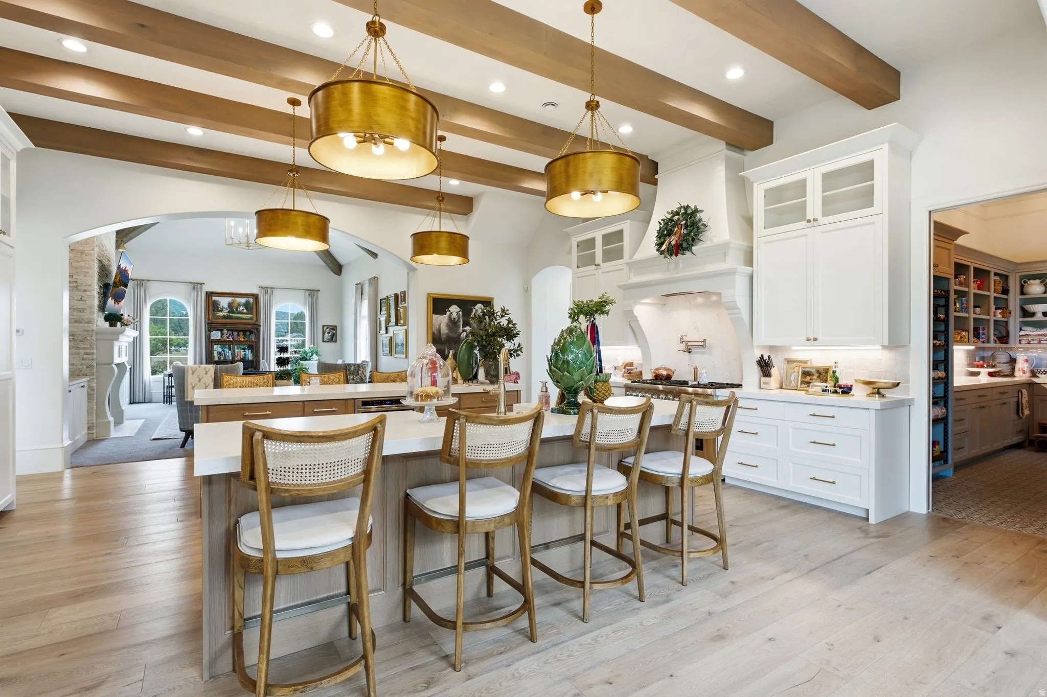Spacious kitchen featuring an expansive central island with seating, exposed wood beam ceiling, contemporary pendant lighting, light wood-finish flooring, and white cabinetry