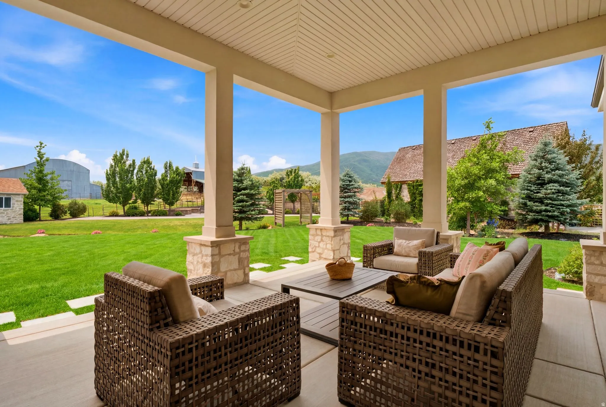 Expansive covered patio featuring a concrete surface, decorative columns with stone bases, and an open-gable ceiling