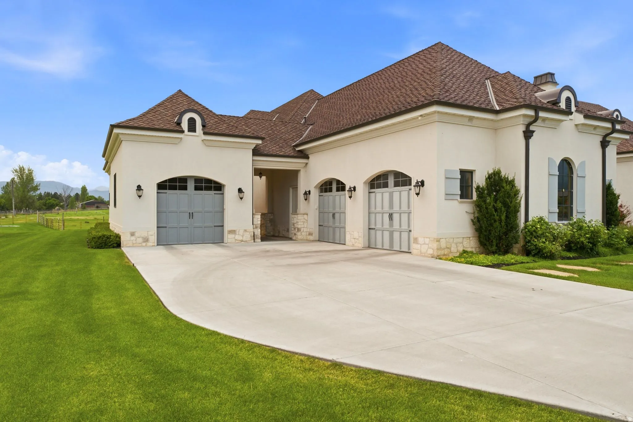 Stucco exterior featuring multiple arched garage doors, a curved concrete driveway, and a shingle roof
