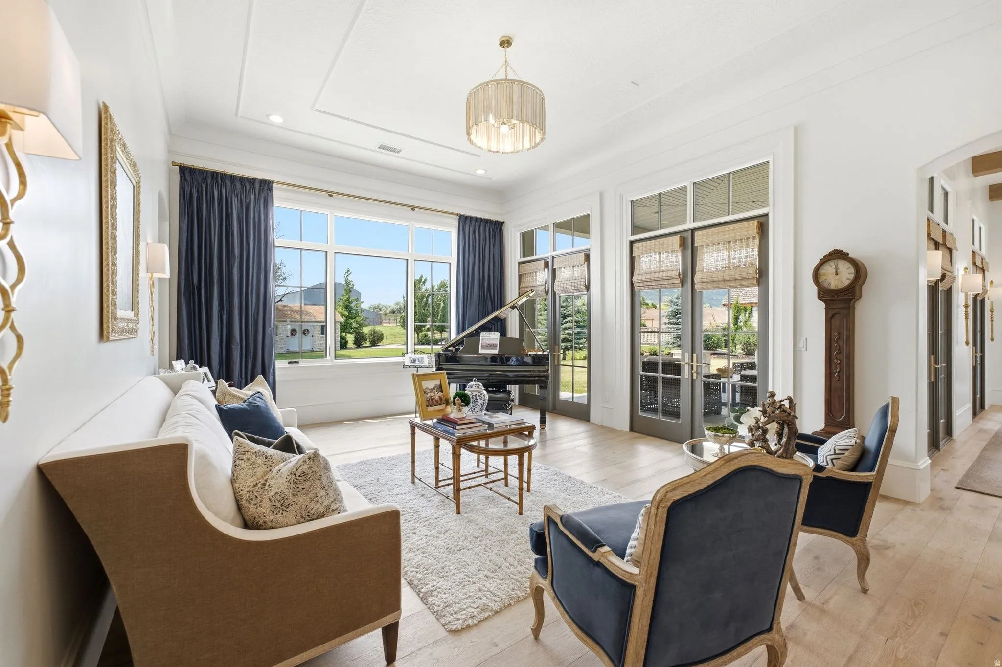 Bright living area featuring wood-finish flooring, white coffered ceilings, large picture windows with dark drapery, and French doors