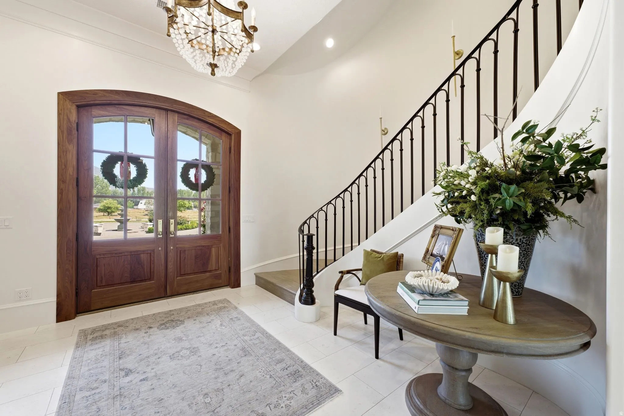 Grand entryway featuring a curved staircase with wrought iron balusters, a large arched wooden double-door entry with divided lites, and a crystal chandelier