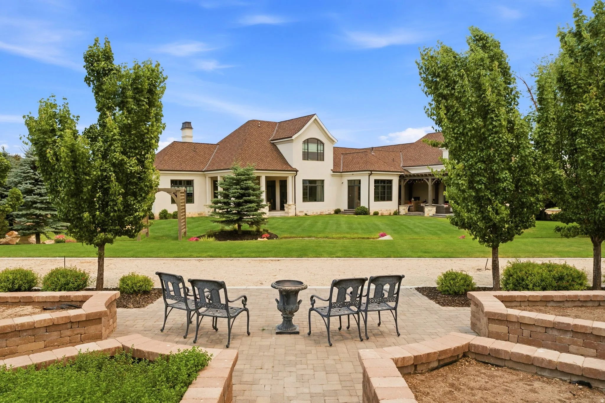 Expansive outdoor patio area featuring paver flooring, curved brick planters, and mature trees