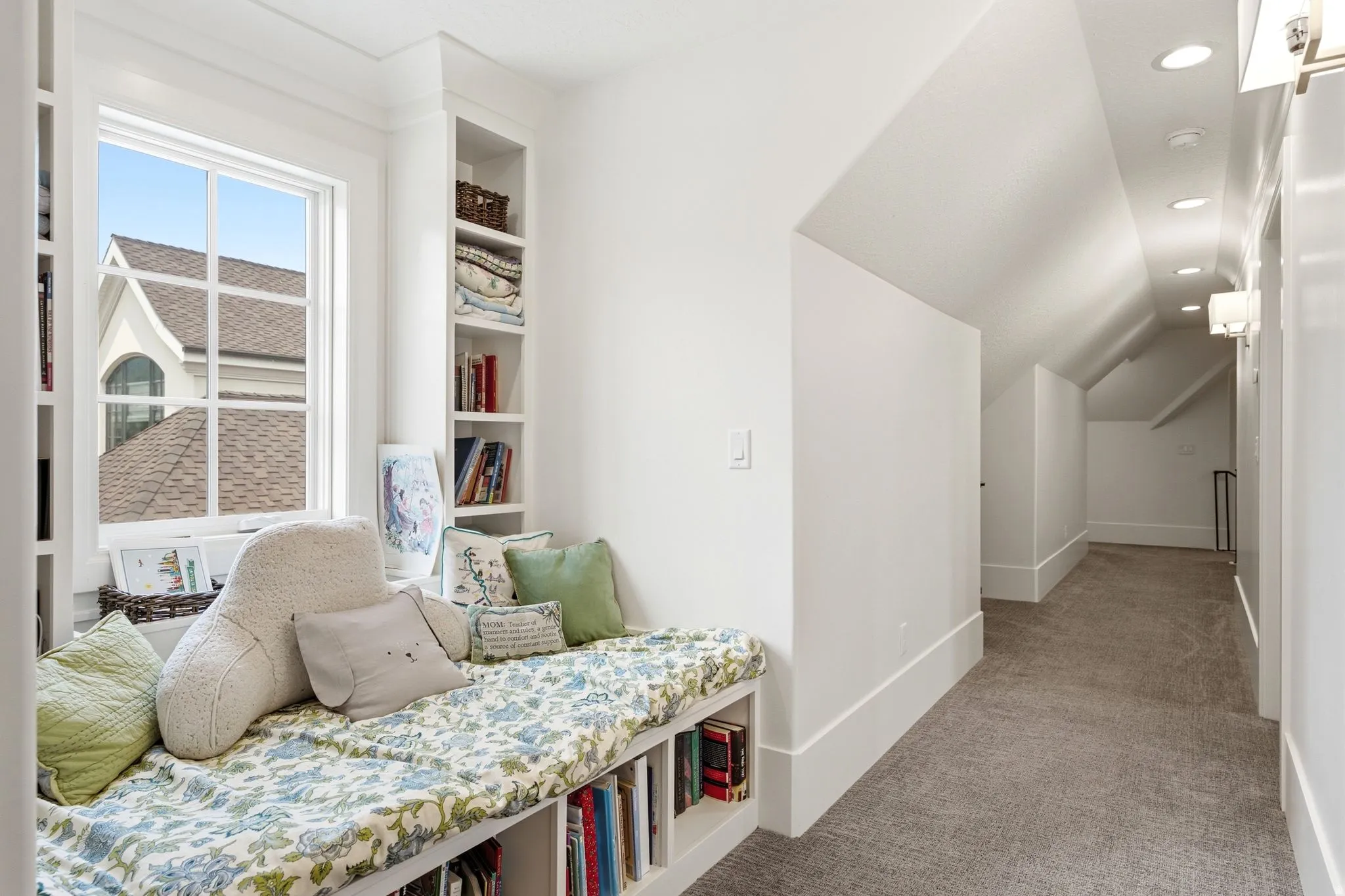 Window seat with integrated shelving, built-in bookcases, recessed lighting, wall sconces, and sloped ceiling details