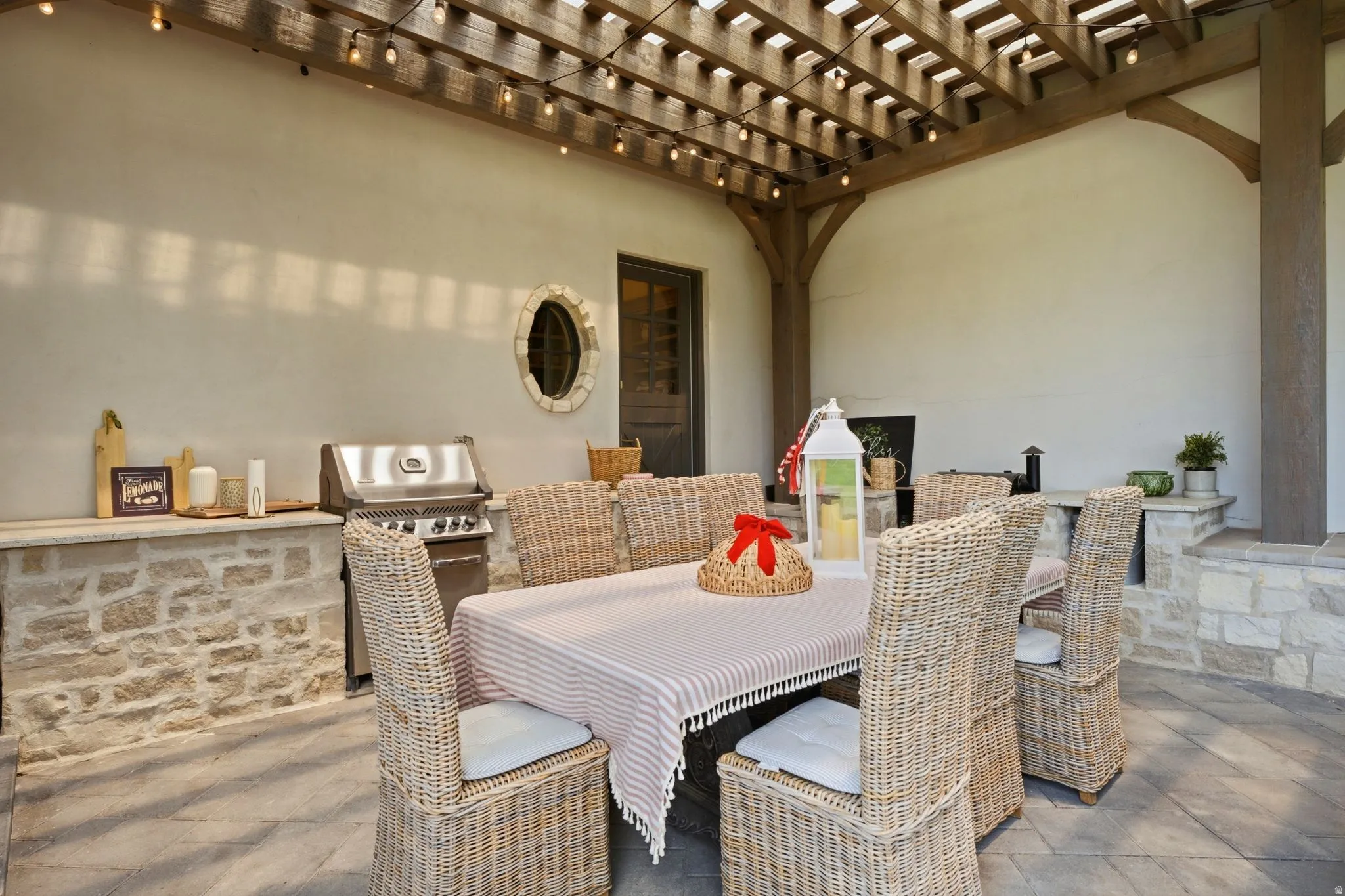 Covered patio featuring a wood pergola with string lighting, stone-clad outdoor kitchen with built-in grill, and stone flooring