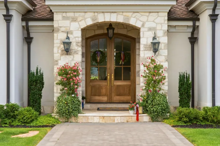 Arched wooden entry doors with glass panels, flanked by stone masonry and sconce lighting