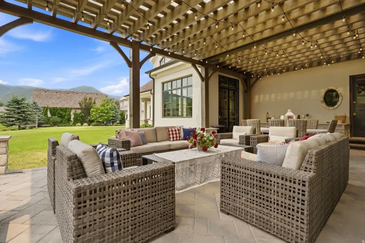 Expansive paver patio with a wooden pergola, string lighting, and ample seating areas