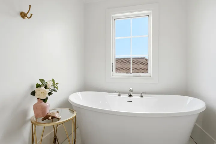 Freestanding soaking tub with polished chrome fixtures, set beneath a white-framed window