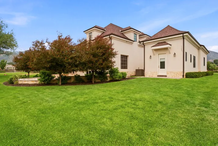 Spacious exterior grounds featuring expansive green lawn, mature trees, stucco facade, stone detailing, and a shingle roof