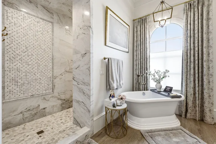 Freestanding pedestal bathtub with a large arched window, complemented by a spacious walk-in shower featuring patterned tile inlay, full-height tile walls, and hexagon tile flooring