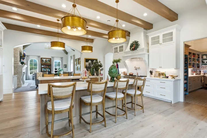 Spacious kitchen featuring an expansive central island with seating, exposed wood beam ceiling, contemporary pendant lighting, light wood-finish flooring, and white cabinetry