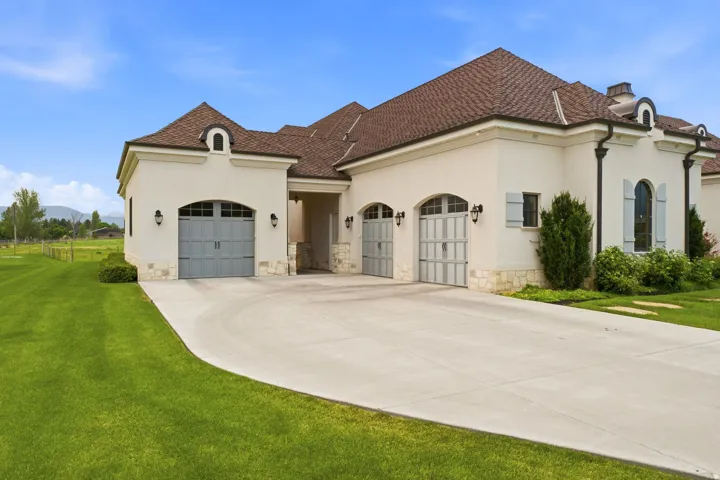 Stucco exterior featuring multiple arched garage doors, a curved concrete driveway, and a shingle roof