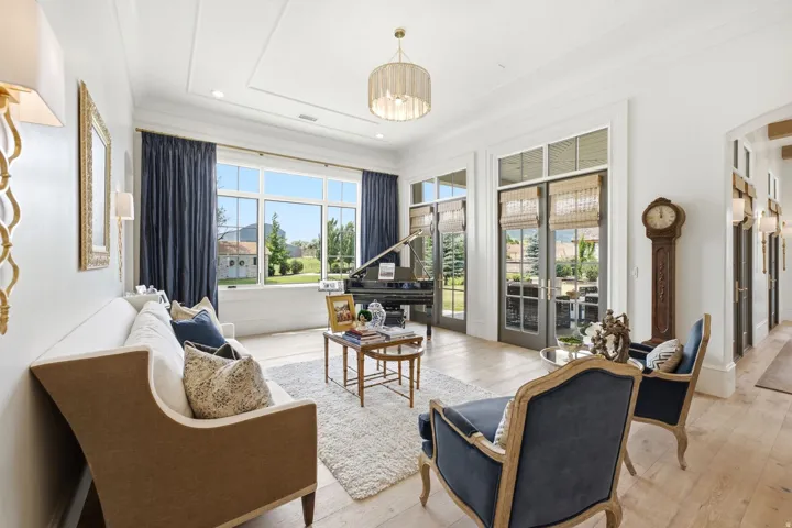 Bright living area featuring wood-finish flooring, white coffered ceilings, large picture windows with dark drapery, and French doors