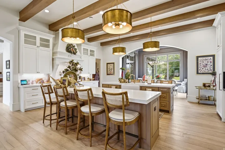 Gourmet kitchen featuring a dual island design, light wood-finish flooring, exposed wood ceiling beams, white cabinetry with glass-front accents, and a built-in range hood